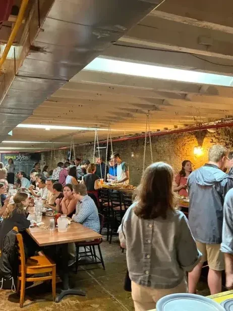 Cozy, bustling restaurant interior filled with people and warm rustic lighting.