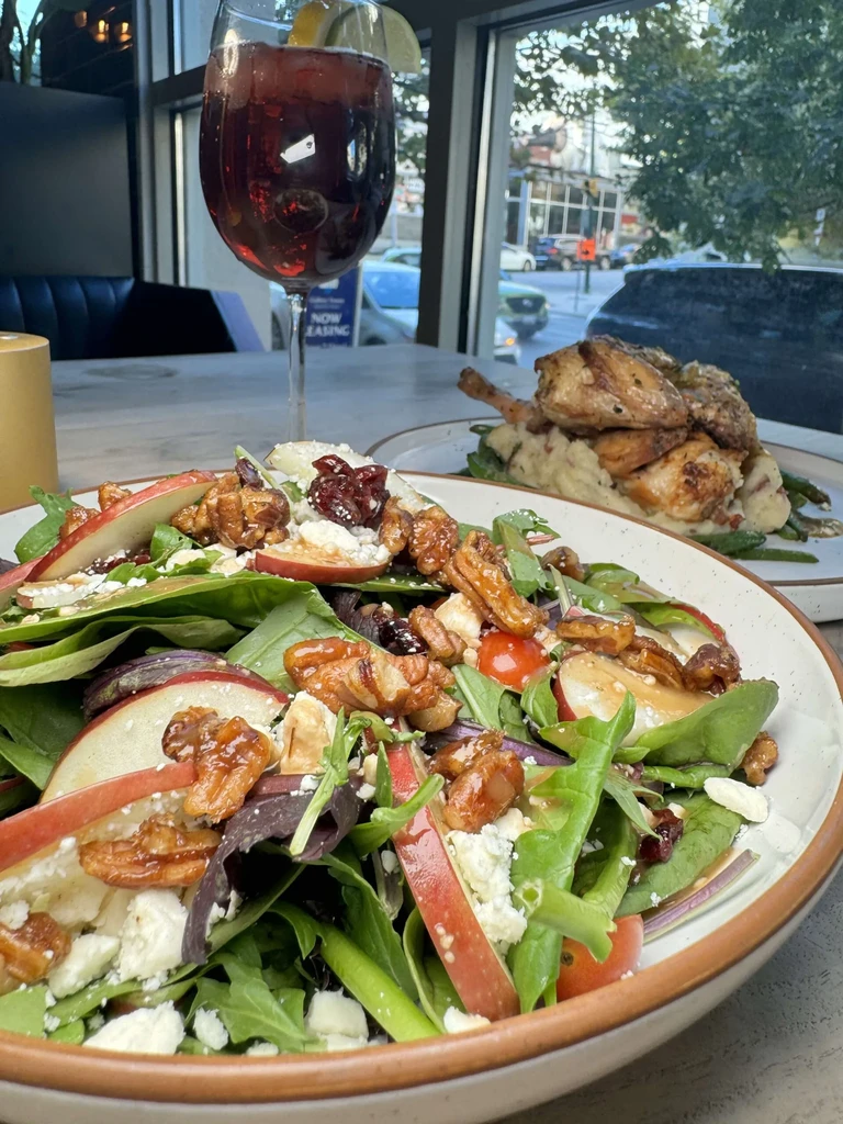 Gourmet salad with apple, cheese, pecans, cranberries; wine glass and chicken in background.