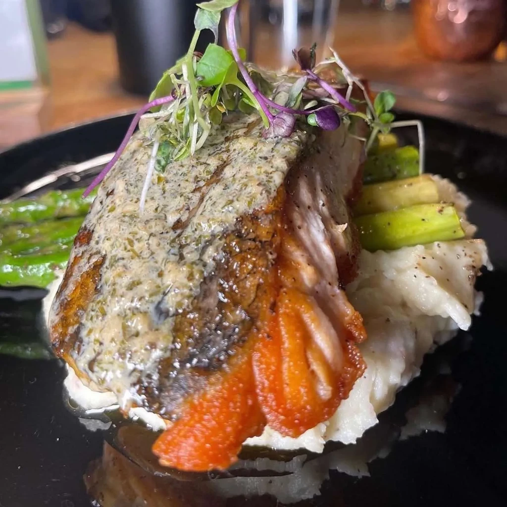 Plated salmon with herb crust, mashed potatoes, asparagus, and microgreens.