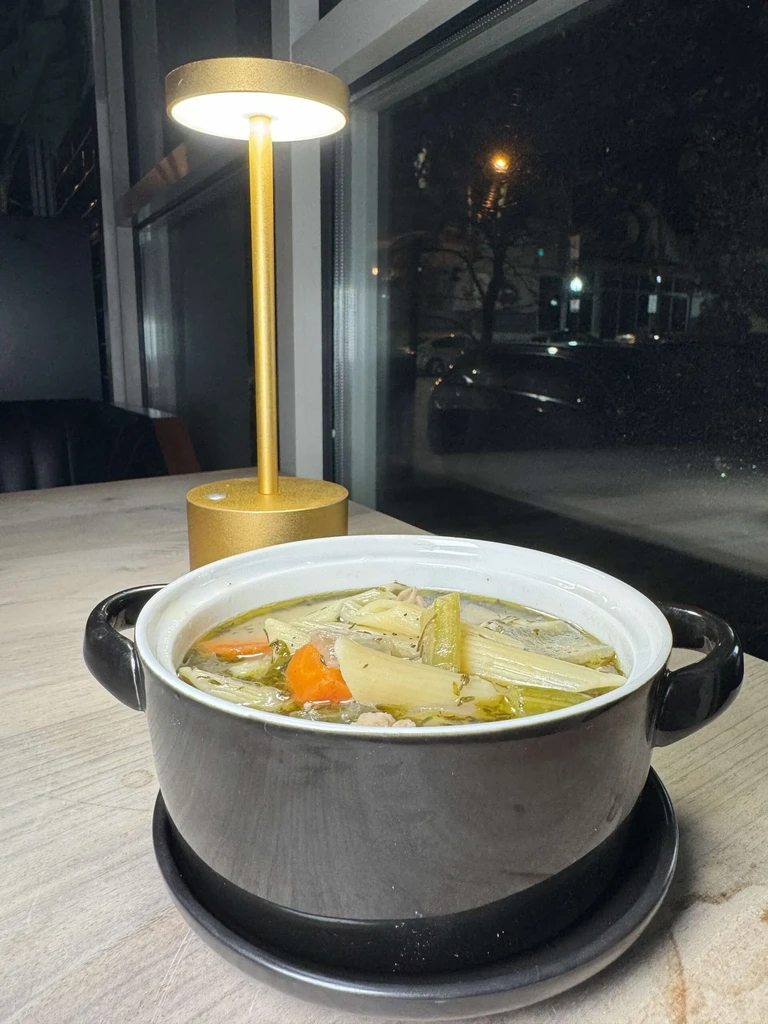 Dark grey pot of vegetable soup with noodles on a wooden table.
