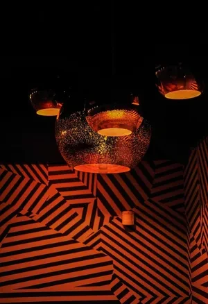 Warm orange pendant lights illuminate a geometric black and orange striped wall.