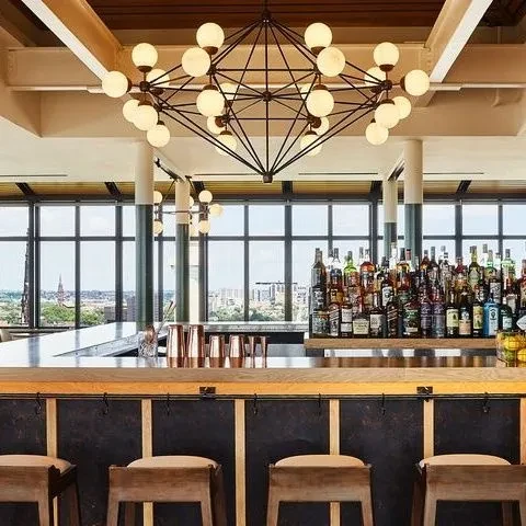 Elevated bar with geometric chandelier, full counter, and panoramic city view.