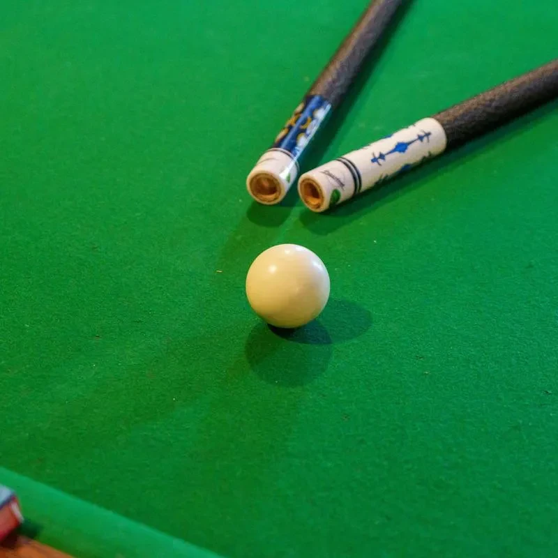 White cue ball and two patterned pool cues on green felt.