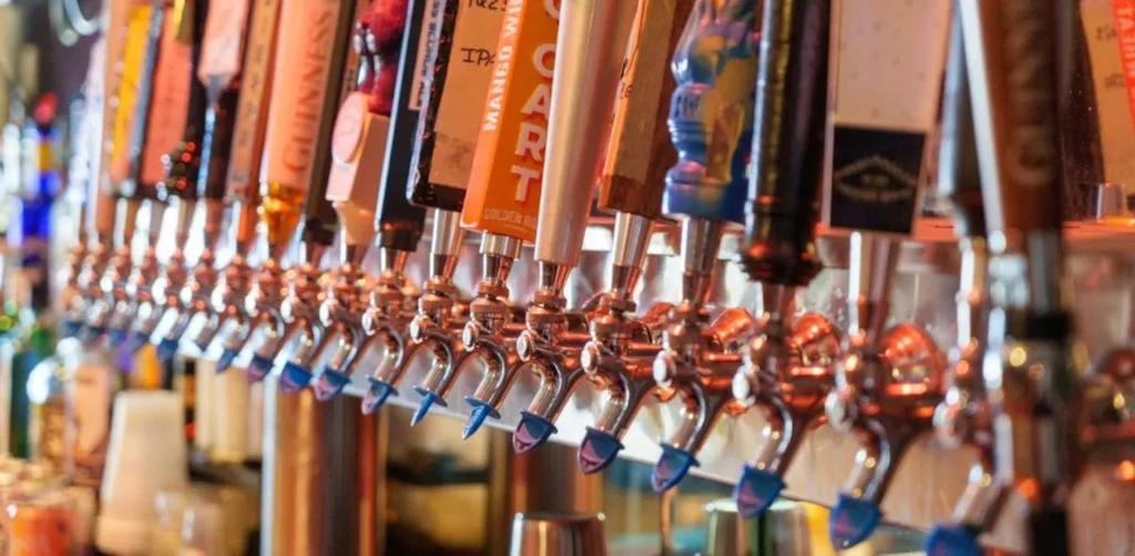 Close-up of a long row of chrome beer taps with brand labels.