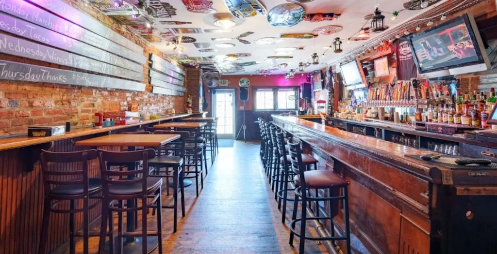 Rustic bar interior with chalkboards, wooden bar, and high-top tables.
