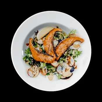 Grilled salmon salad with greens and vegetables on a white plate.