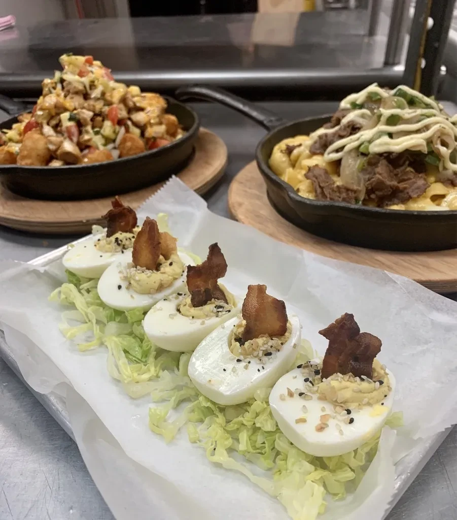 Deviled eggs with everything bagel seasoning and bacon, blurred dishes in kitchen.