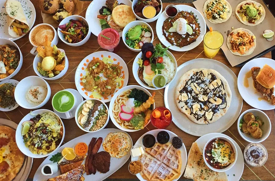 Large wooden table laden with diverse breakfast, brunch, and lunch dishes.