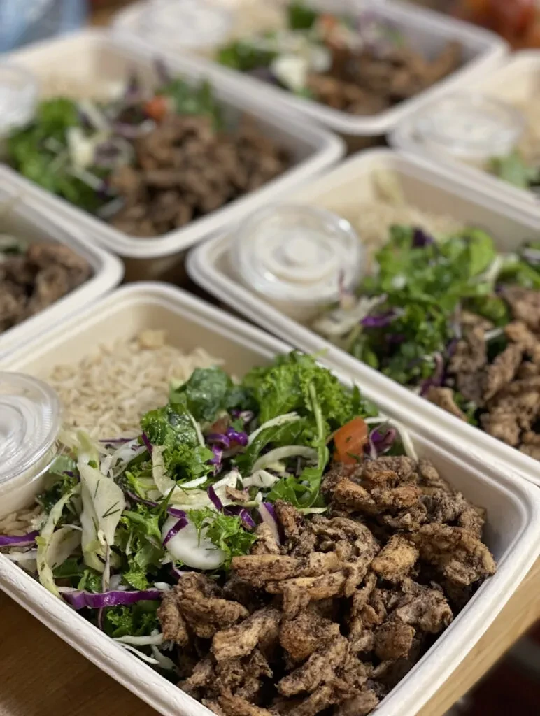 Grid of takeout meal bowls: rice, salad, meat, and sauce.