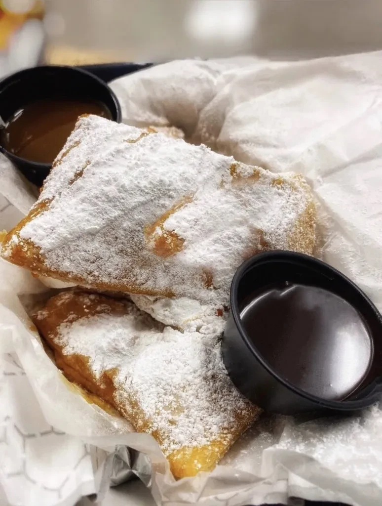 Fried dough pastries dusted with powdered sugar, served with caramel and chocolate sauces.