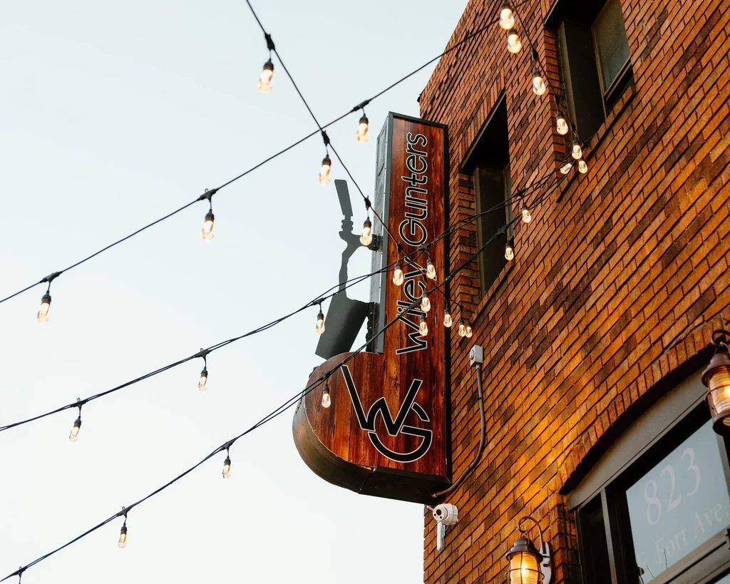 Vertical dark wood 'Wiley Gunters' sign on a reddish-brown brick building.