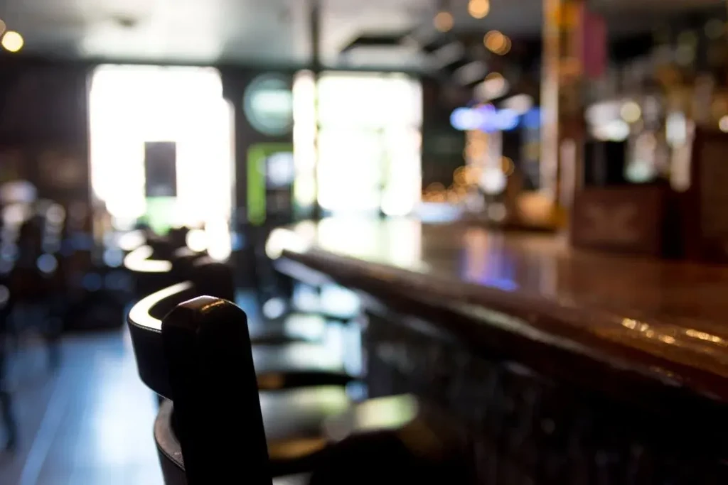 Dark bar stool and polished wooden counter before blurred bright windows.