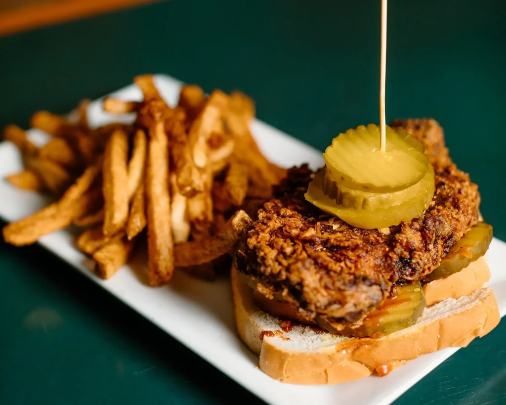 Crispy fried chicken sandwich, pickles, and fries on a white plate.