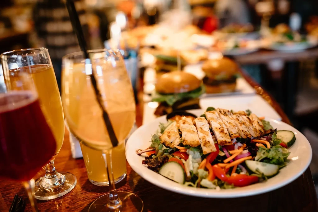 Fresh grilled chicken salad, drinks, and blurred burgers in a restaurant.