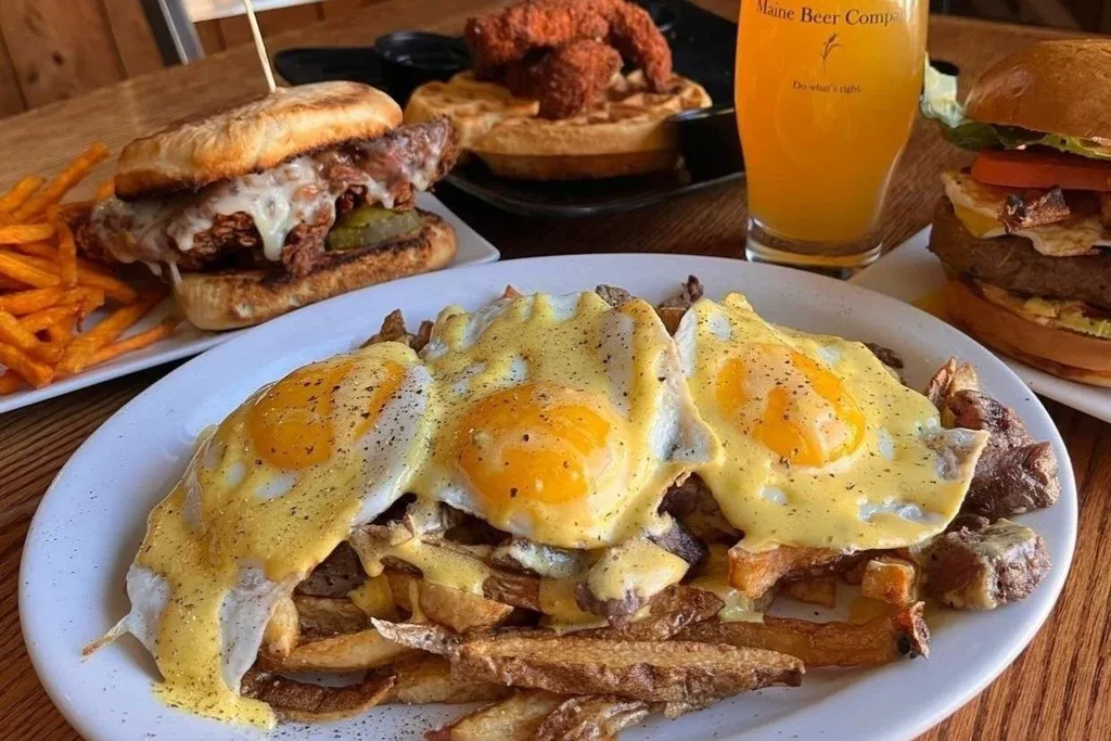 Steak, fries, eggs with hollandaise, a sandwich, and beer on a table.