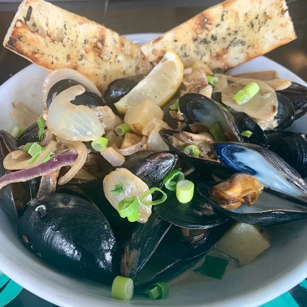 Steamed mussels in a bowl with onions, lemon, and herb bread.