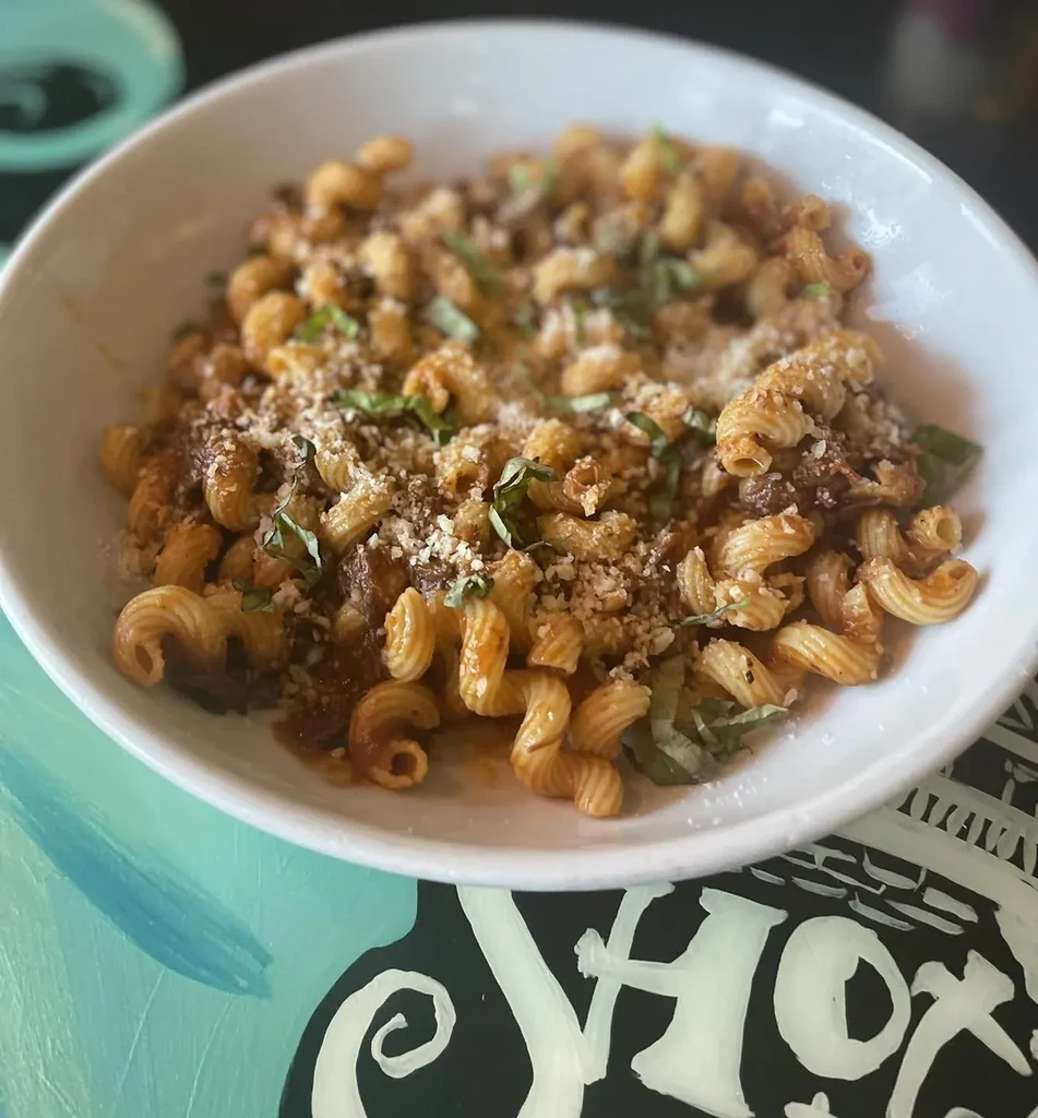 Corkscrew pasta, sauce, cheese, basil in bowl on artistic table.