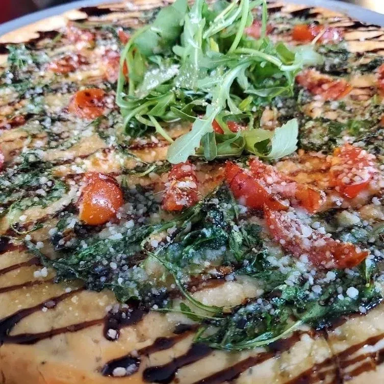 Arugula, cherry tomatoes, and cheese pizza with balsamic glaze.