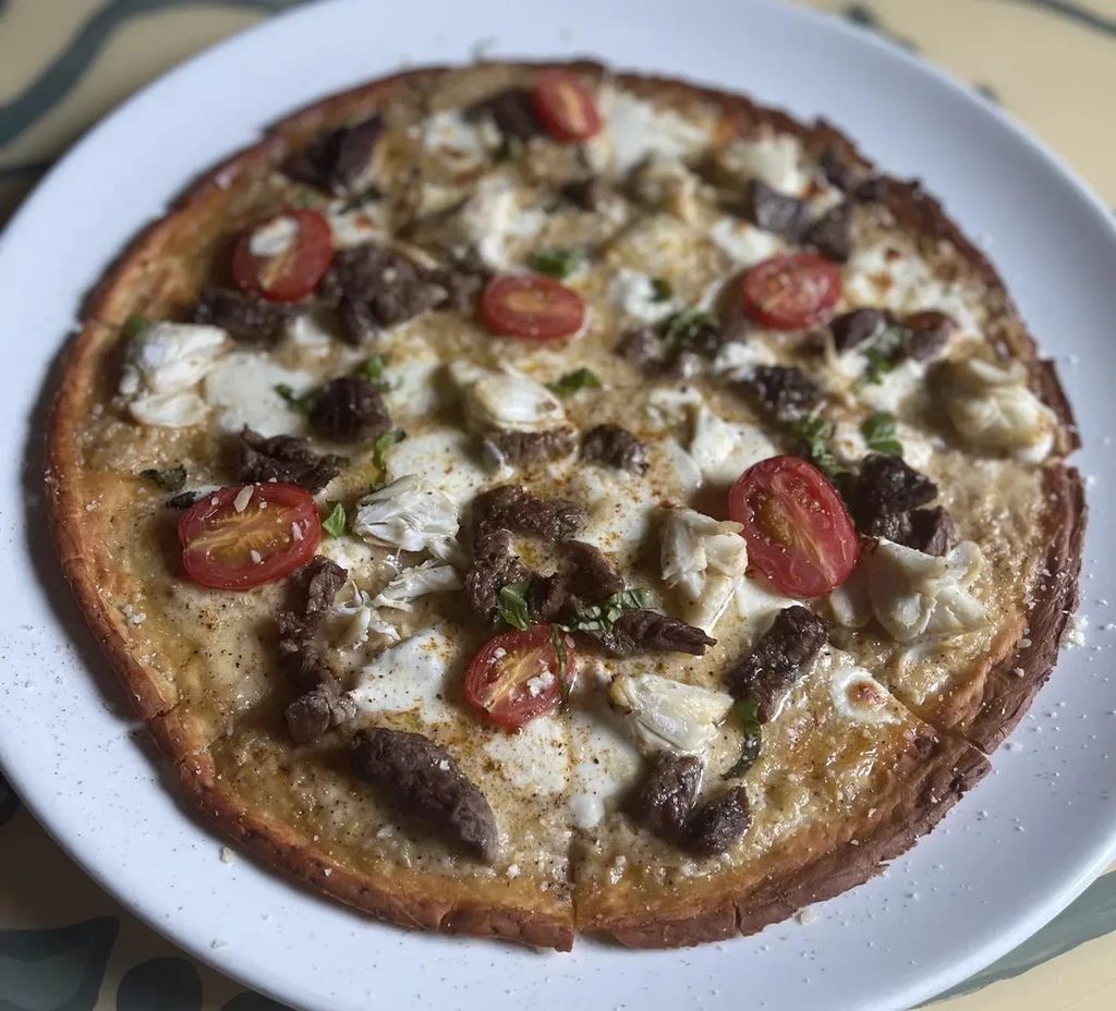 Sliced pizza with dark meat, mozzarella, cherry tomatoes, and herbs.