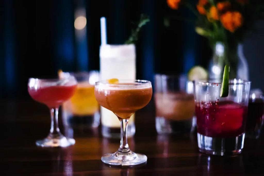 Various cocktails, an amber drink in focus, on a dark wooden surface.