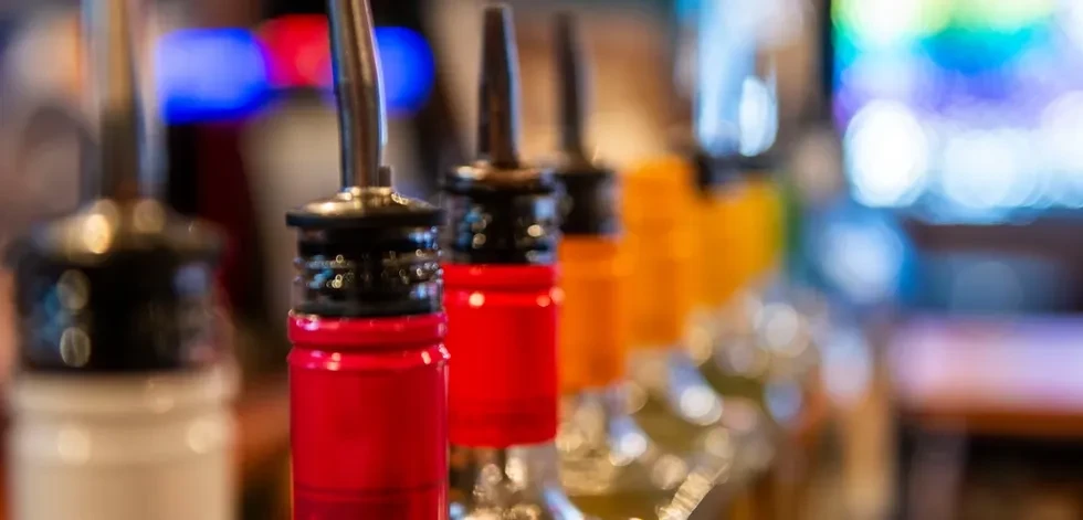 Close-up of red liquor bottle with pourer, blurred bar background.