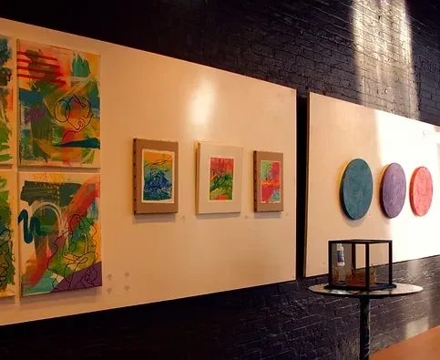 Gallery wall with diverse abstract art on white panels, dark brick.