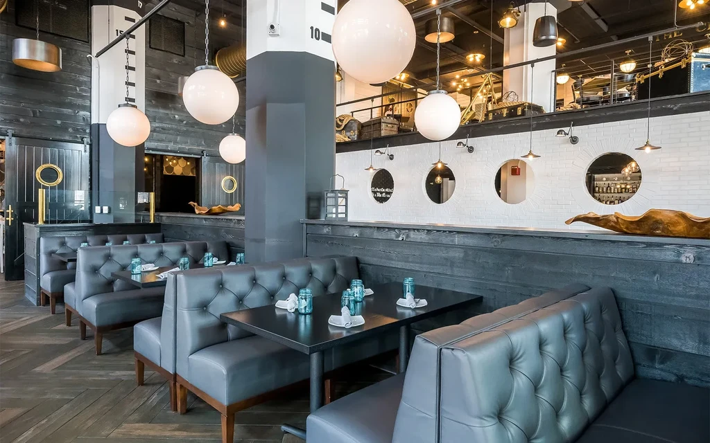 Modern nautical-industrial restaurant interior with dark booths and porthole windows.