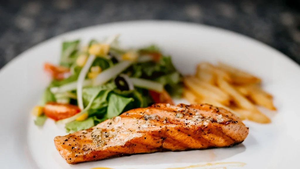 Plate of grilled salmon, green salad, and french fries.