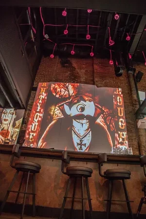 Dimly lit bar with stools and large illuminated macabre character sign.