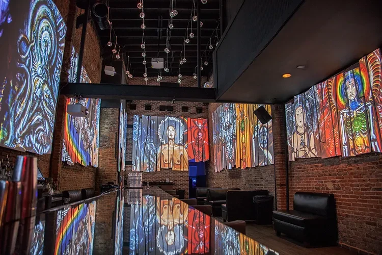 Modern bar with reflective black counter, red brick, and projected abstract art.