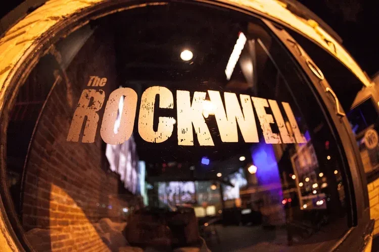Distressed "The ROCKWELL" name on dark venue's glass, fisheye perspective.