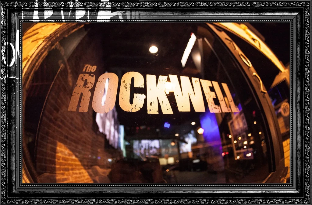 Framed fisheye view of 'THE ROCKWELL' entrance with urban night reflections.