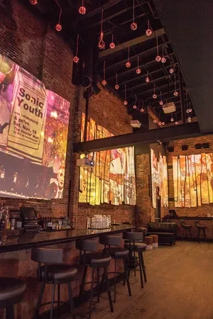 Modern bar interior with brick walls, dark counter, Sonic Youth projection.