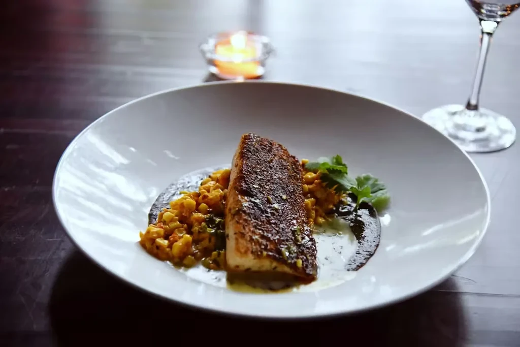 Crispy pan-seared fish on corn succotash with sauces and garnish.