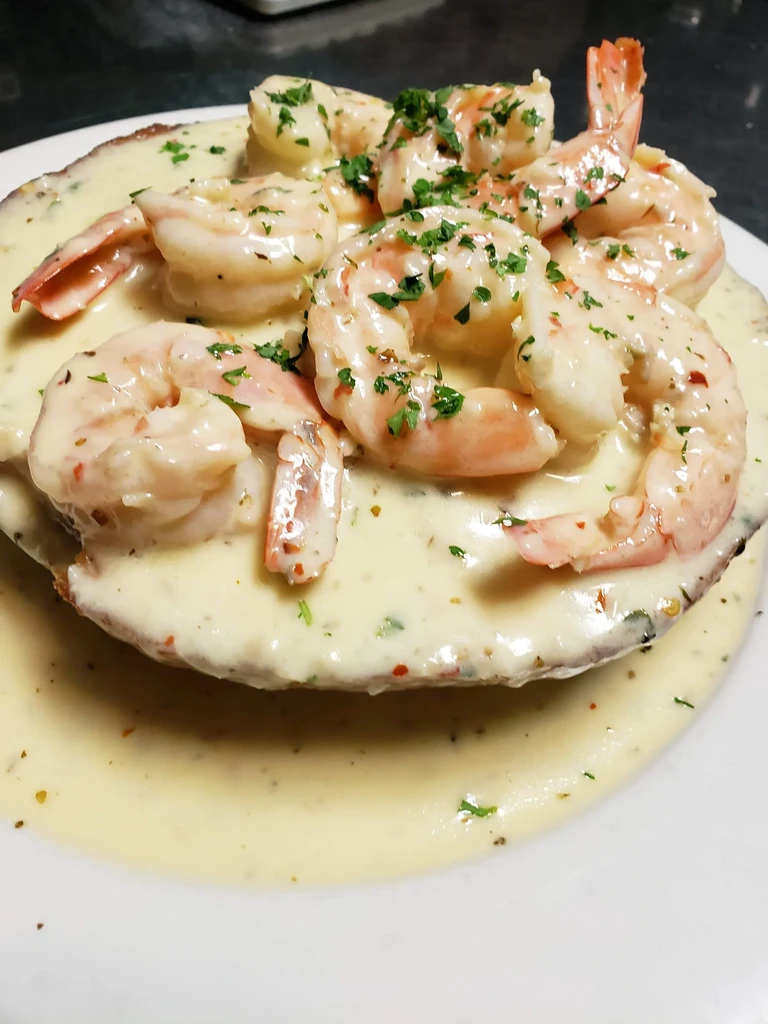 Cooked pinkish-orange shrimp on creamy herb sauce with base.