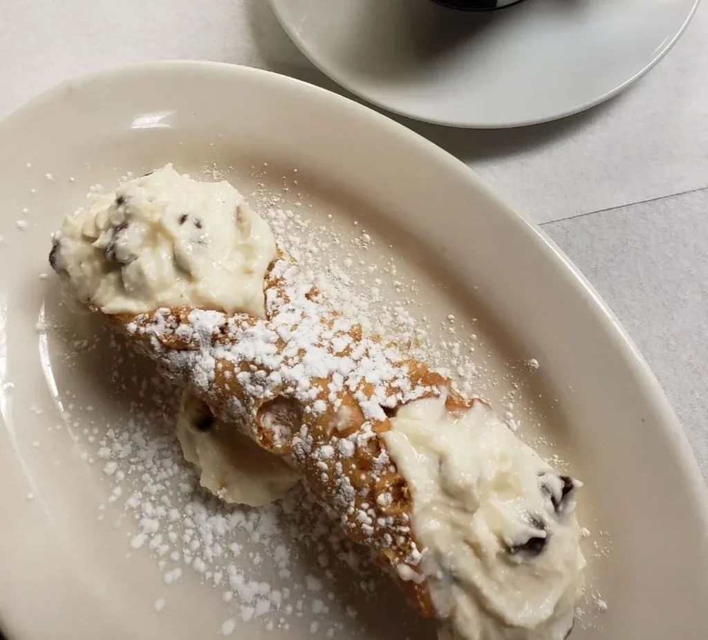 Powdered sugar-dusted cannoli with chocolate chip ricotta filling on a white plate.