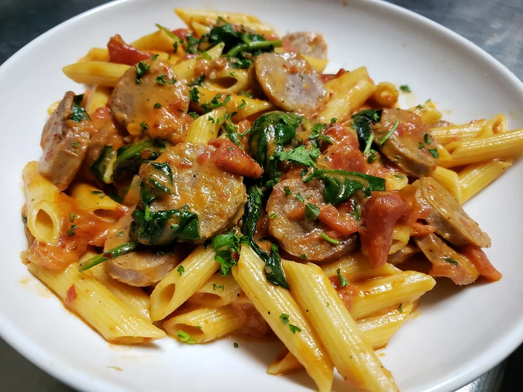 Close-up of penne pasta with sausage, tomato sauce, and spinach.