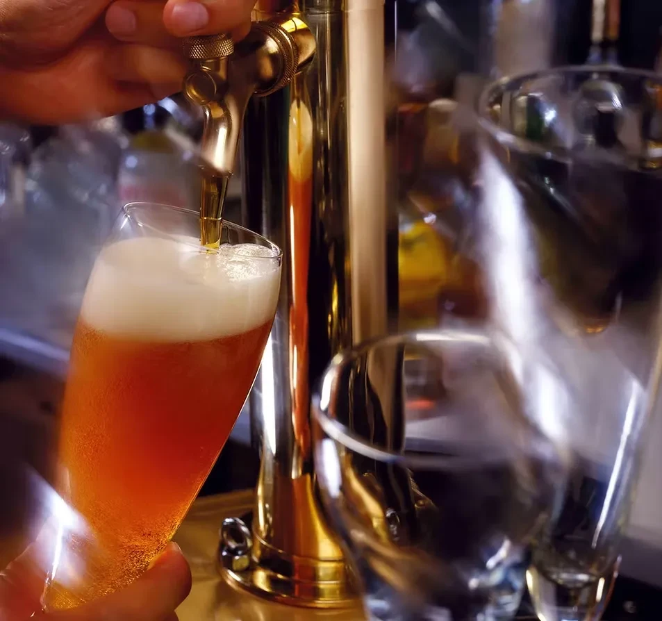 Golden beer with foamy head pours from brass tap into glass.