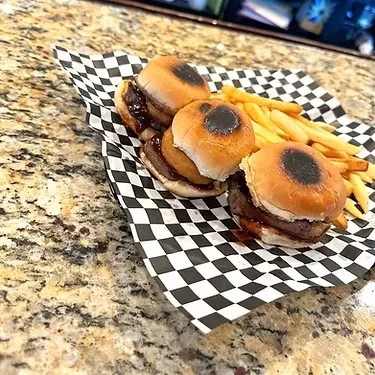 Three sliders, one with onion ring, and fries on checkered paper.