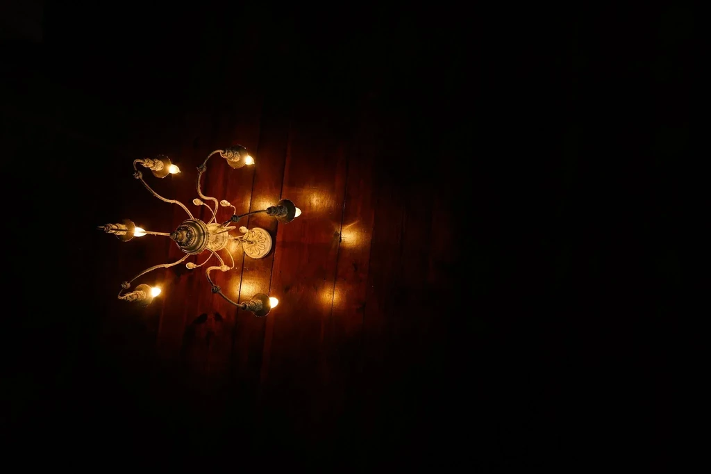 Ornate antique chandelier with six illuminated arms against a dark background.