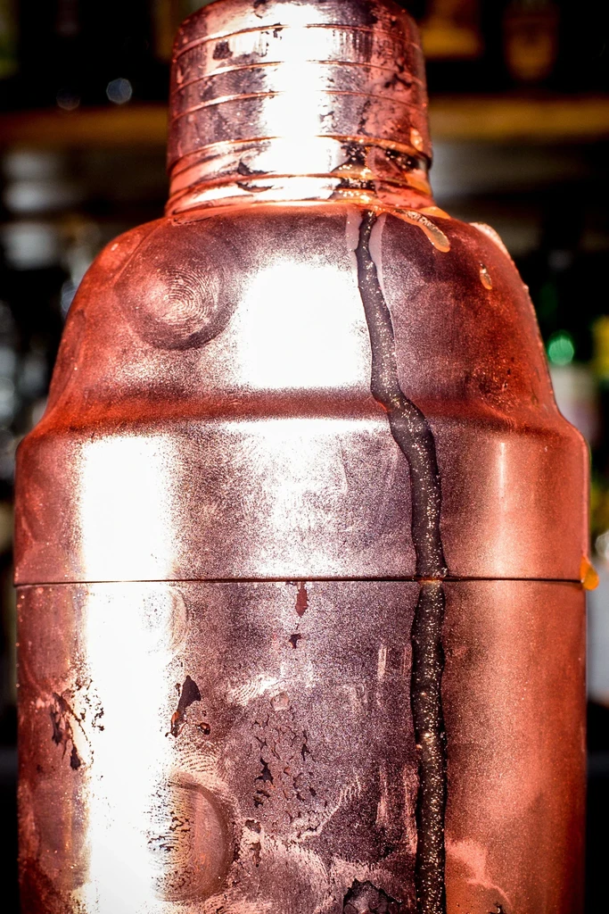 Textured copper cocktail shaker with condensation, a dark streak, and fingerprints.