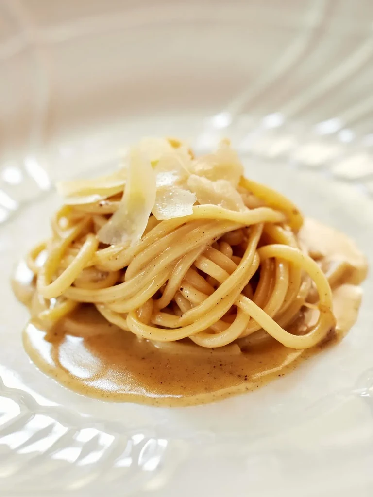 Close-up of creamy pasta with parmesan shavings on a white plate.
