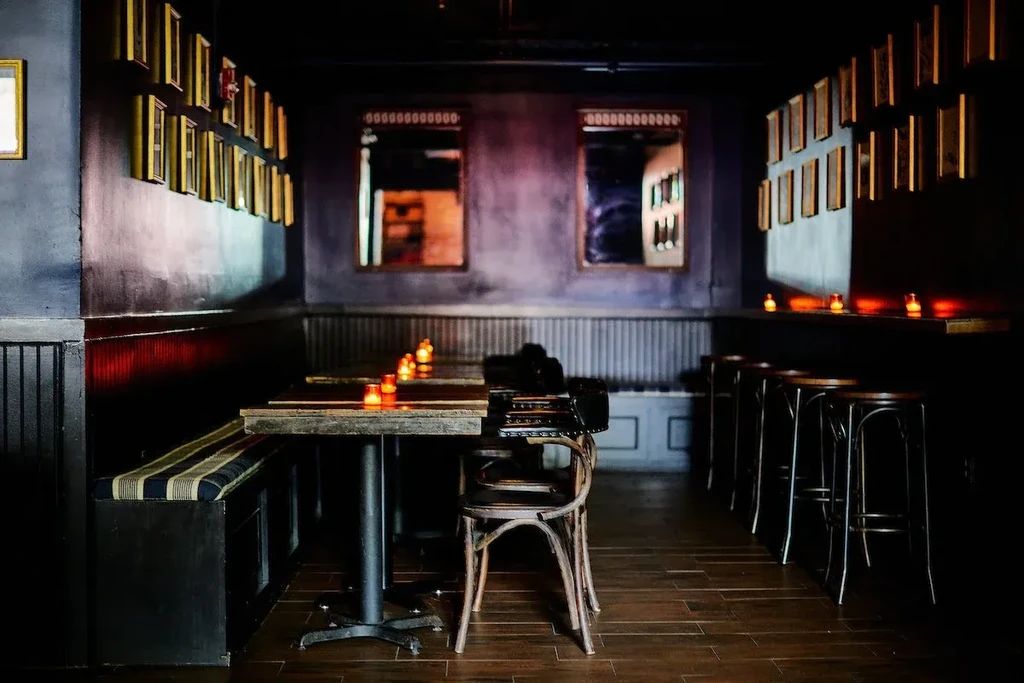 Dimly lit restaurant with dark wood furniture, striped bench, and candles.