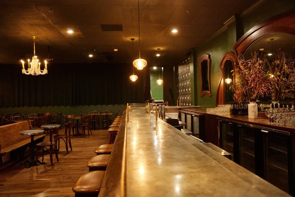 Luxurious bar interior featuring a long counter, leather stools, and green walls.