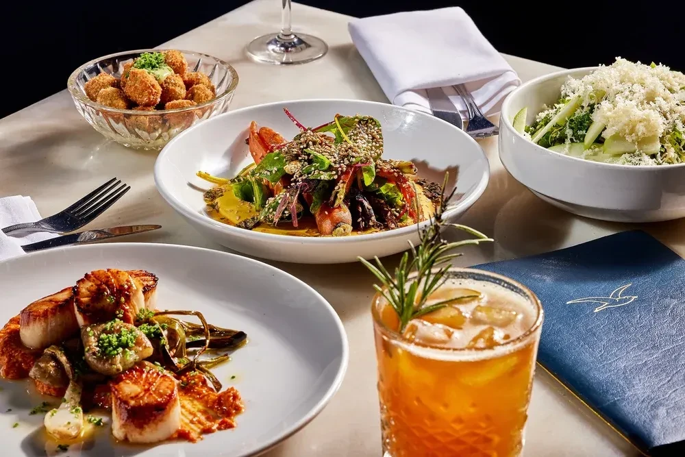 Gourmet dishes and a cocktail on an elegantly arranged fine dining table.