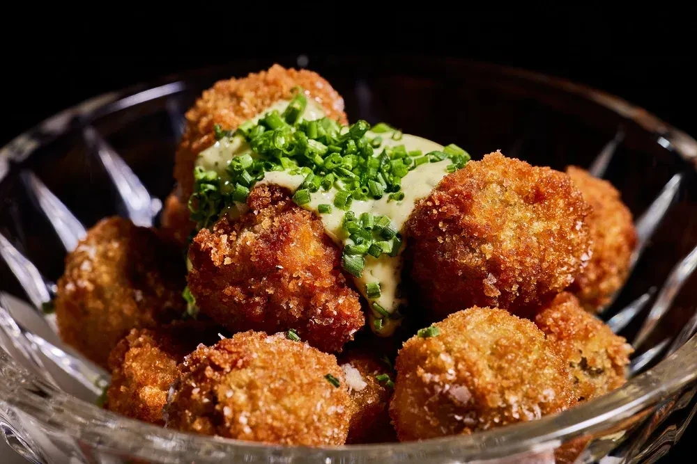Golden fried croquettes with creamy green sauce and chives in a glass bowl.