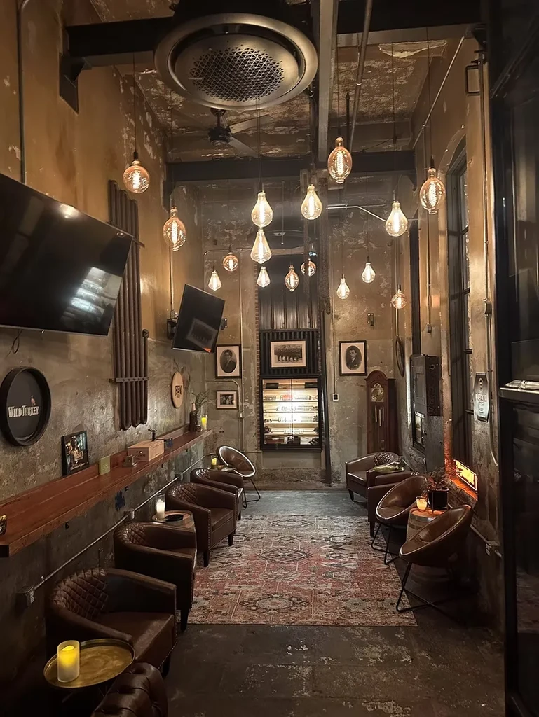 Speakeasy-style bar interior with exposed beams, Edison bulbs, and leather chairs.