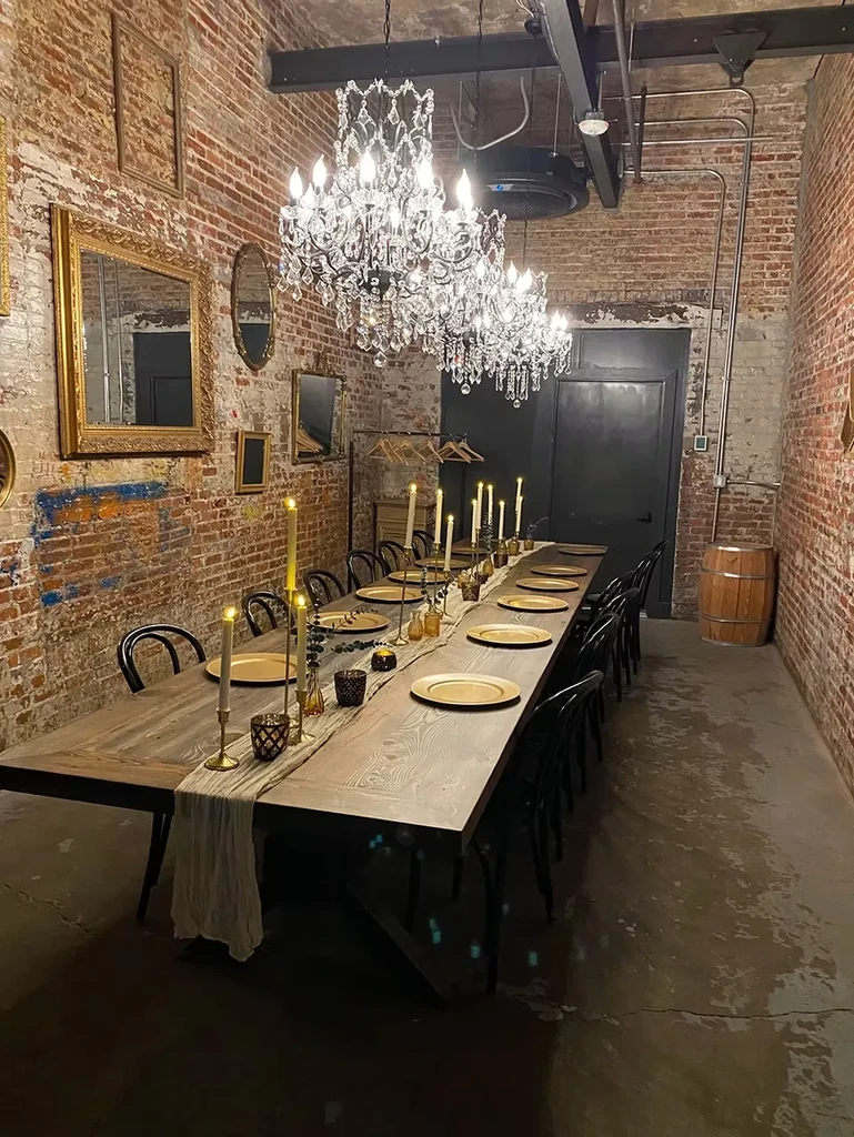 Long brick dining room with crystal chandeliers and candlelit communal table.
