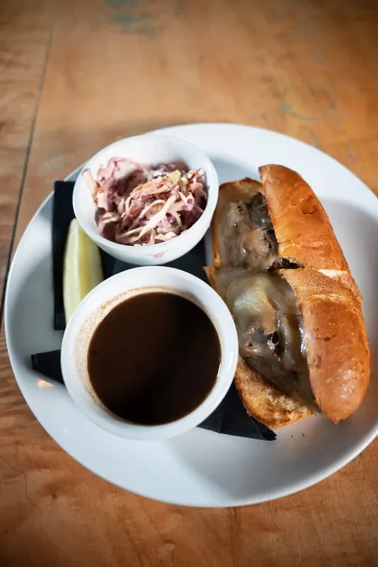 French dip sandwich, melted cheese, coleslaw, au jus, and pickle spear.