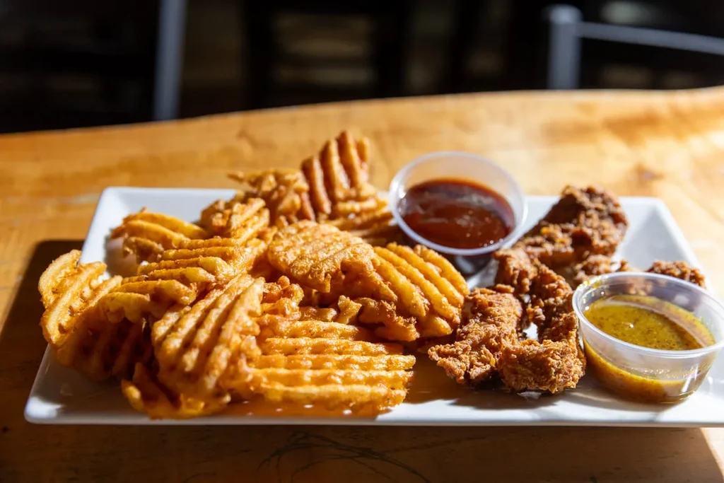 Fried chicken tenders, waffle fries, and two dipping sauces on a plate.